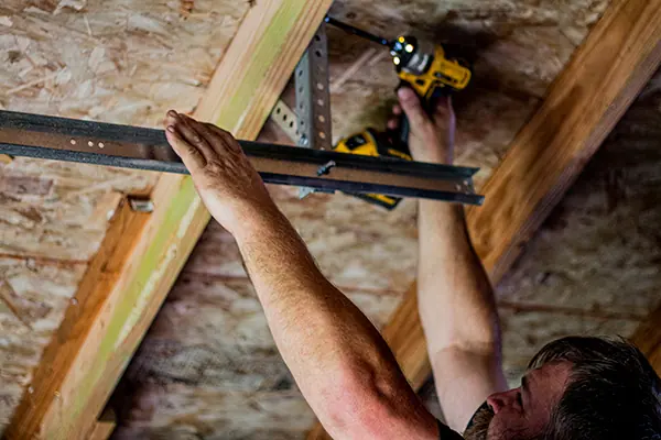 An installer fastening a garage door track to the ceiling framing