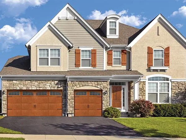 Woodgrain raised-panel garage doors on a stone and siding home